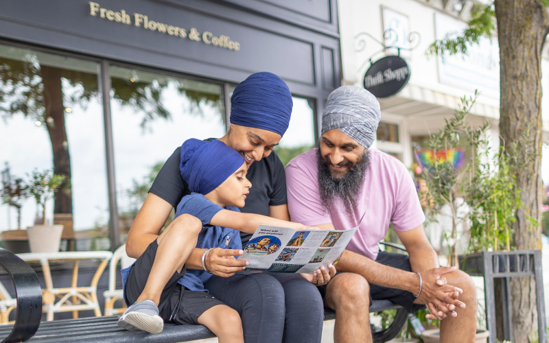 A Sikh family sitting on a bench looking at a brochure.